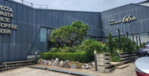낮의 66티에이치 건물 — 벽 글씨와 'Café Restaurant 66th' 간판, 소나무와 정원석